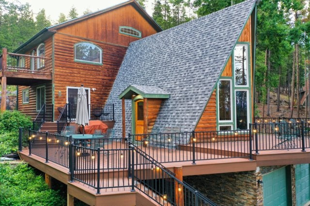 The Evergreen Aerie A-frame cabin at dusk, with a lit wraparound deck surrounded by pine forest