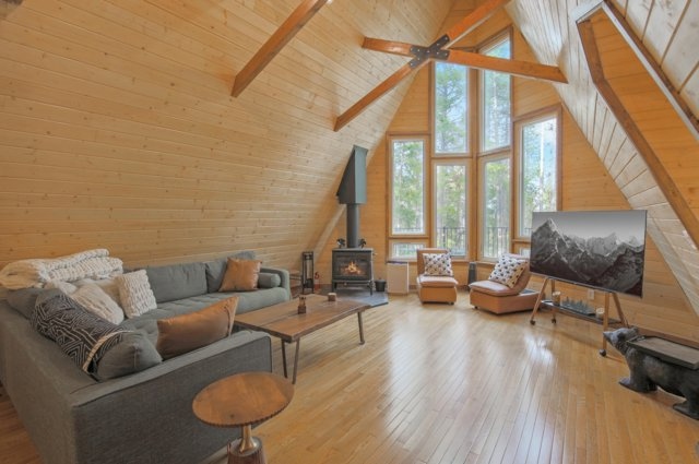 Great room with wood stove, vaulted ceiling, and floor-to-ceiling windows